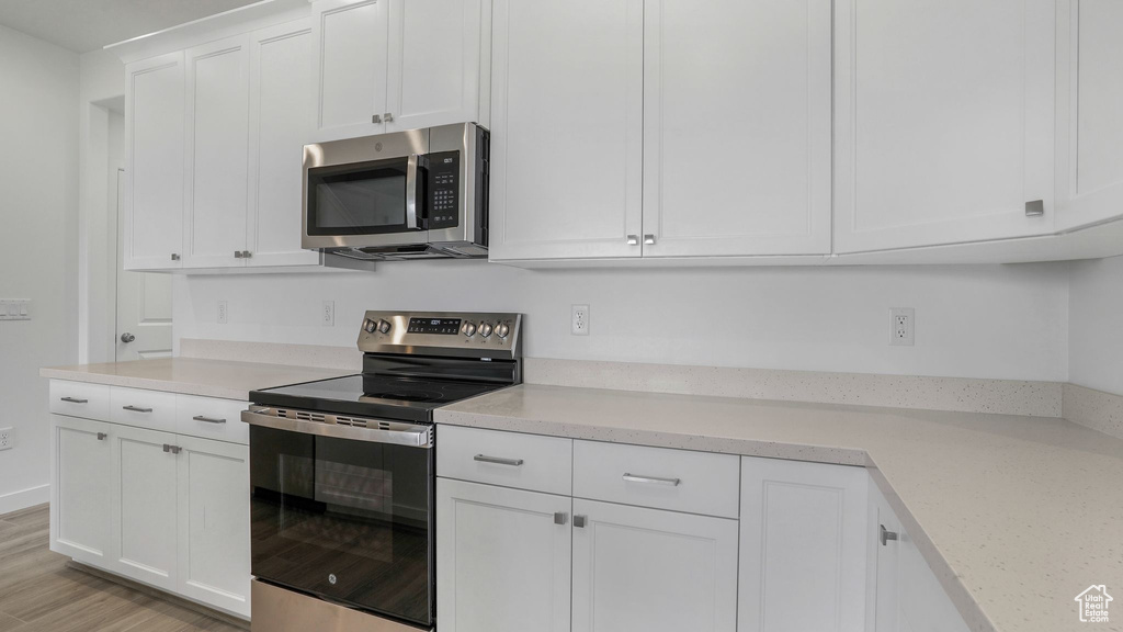 Kitchen featuring appliances with stainless steel finishes, light countertops, white cabinets, and light wood-style flooring