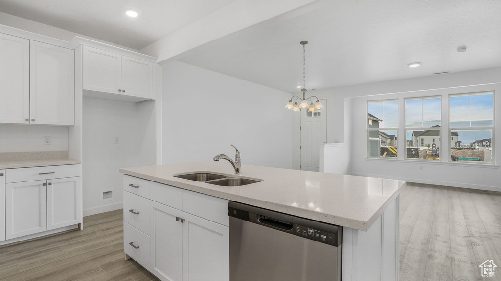 Kitchen with stainless steel dishwasher, a sink, light wood-style floors, white cabinetry, and decorative light fixtures