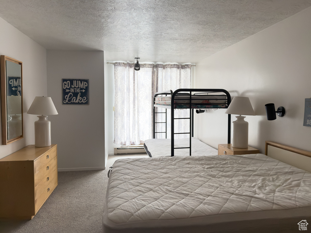 Carpeted bedroom featuring multiple windows, a baseboard heating unit, and a textured ceiling