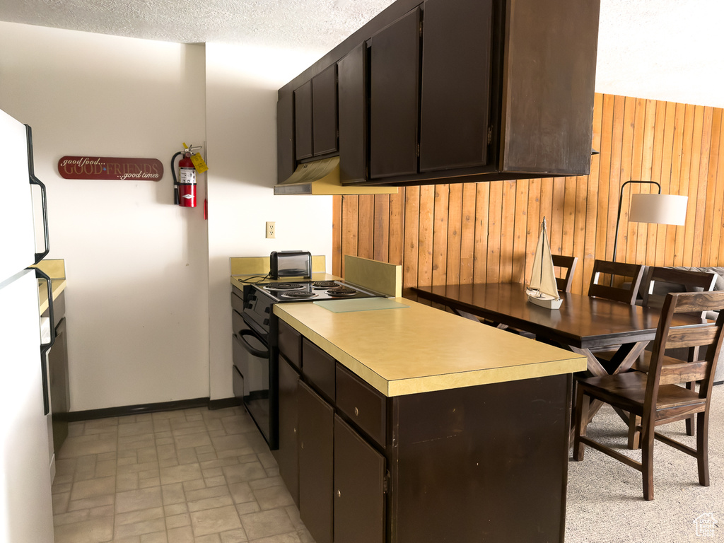 Kitchen with white refrigerator, dark brown cabinets, electric range oven, and wood walls