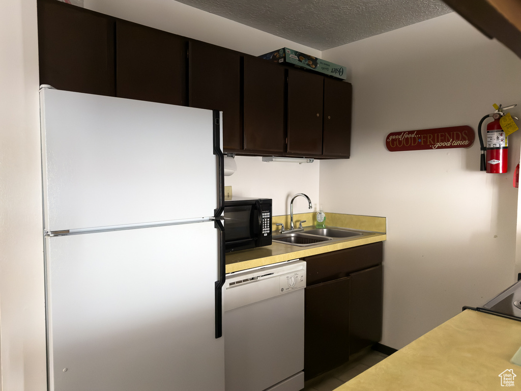 Kitchen with sink, white appliances, dark brown cabinets, and a textured ceiling