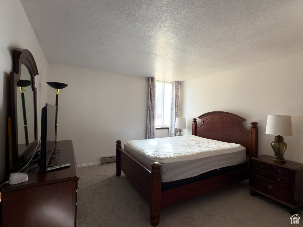 Bedroom with a baseboard heating unit, a textured ceiling, and carpet