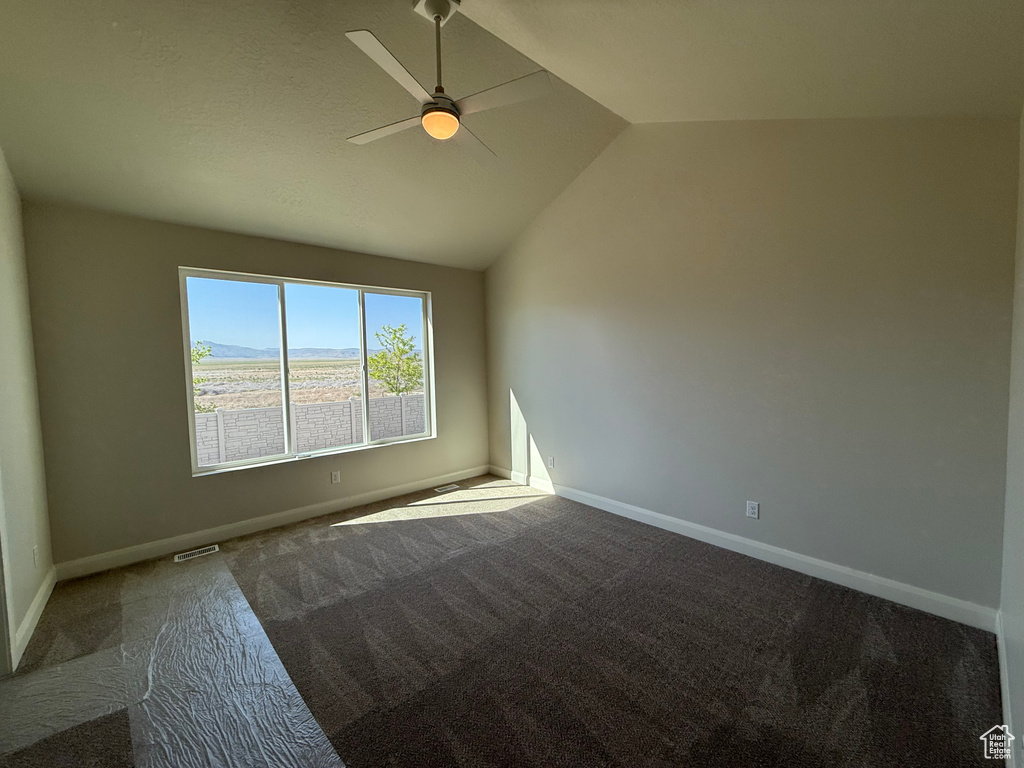 Carpeted spare room featuring vaulted ceiling, a ceiling fan, and baseboards