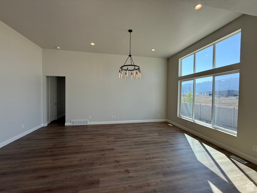 Empty room featuring a chandelier, baseboards, dark wood finished floors, and recessed lighting