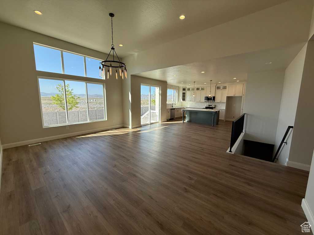 Unfurnished living room featuring a chandelier, recessed lighting, dark wood-type flooring, and baseboards