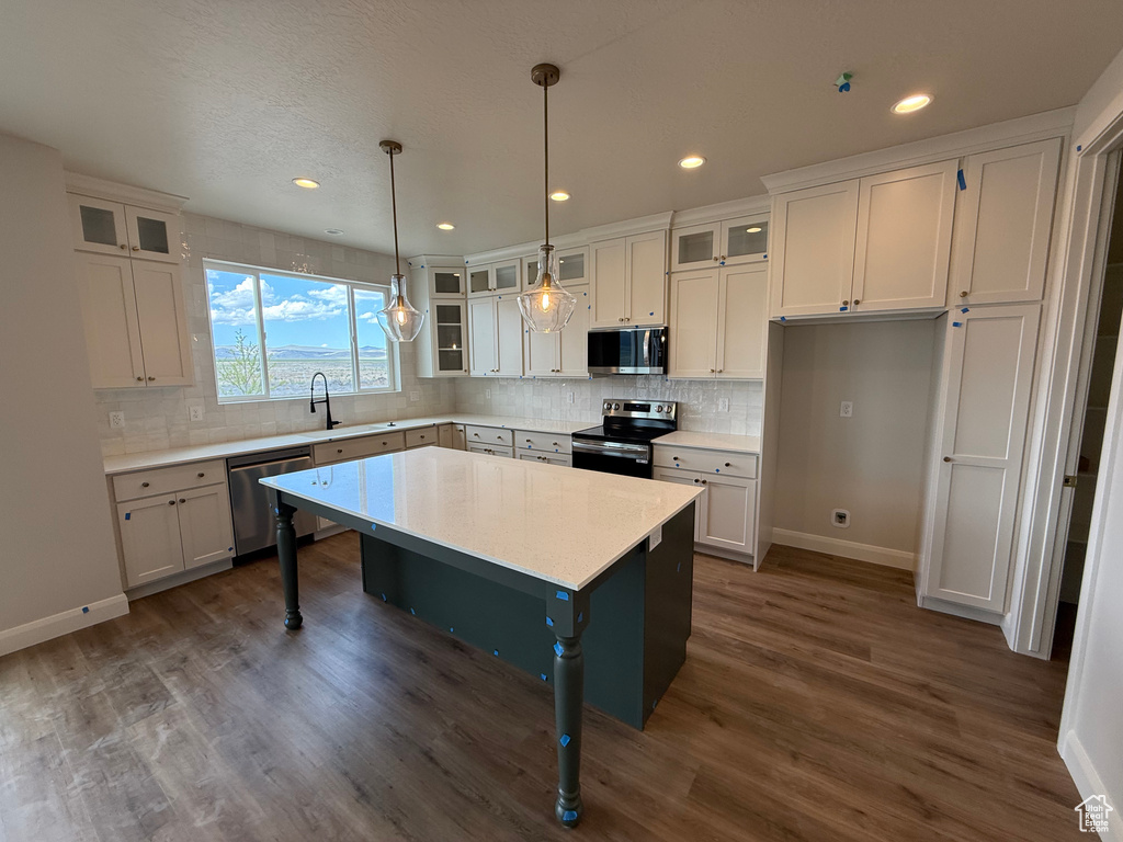 Kitchen featuring appliances with stainless steel finishes, baseboards, dark wood-style floors, white cabinets, and tasteful backsplash
