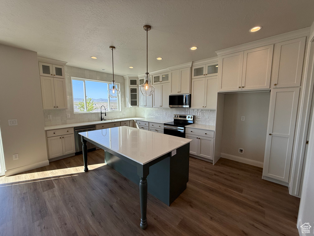 Kitchen with appliances with stainless steel finishes, baseboards, dark wood finished floors, white cabinets, and recessed lighting