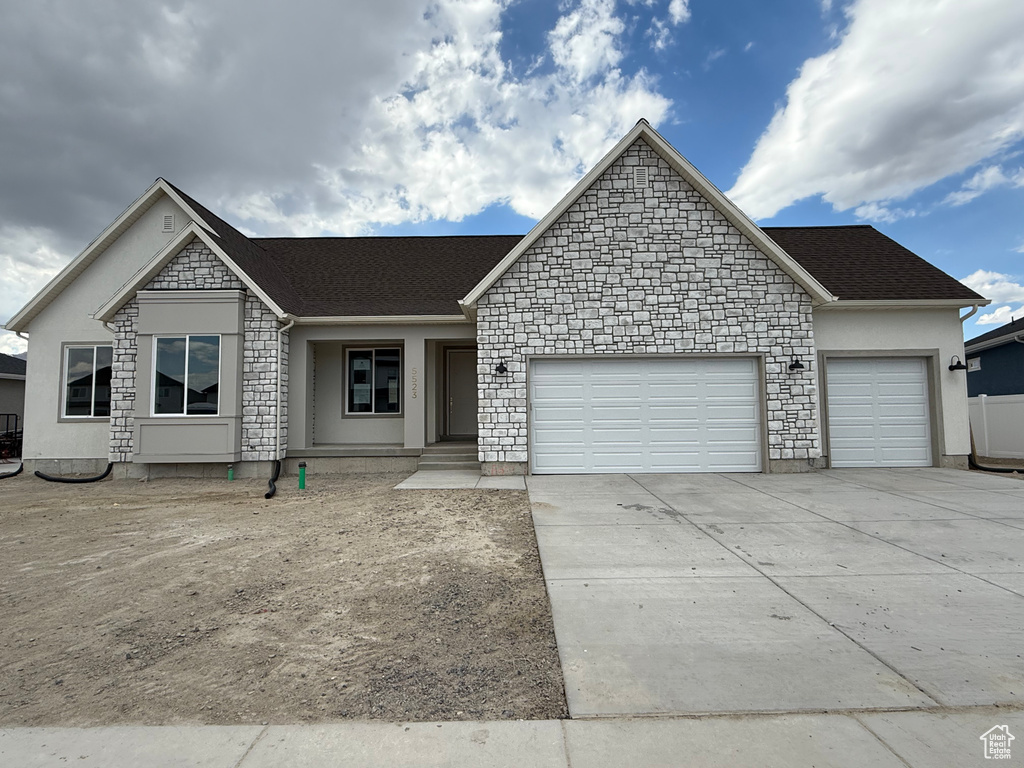 View of front of property featuring an attached garage, driveway, stone siding, and stucco siding