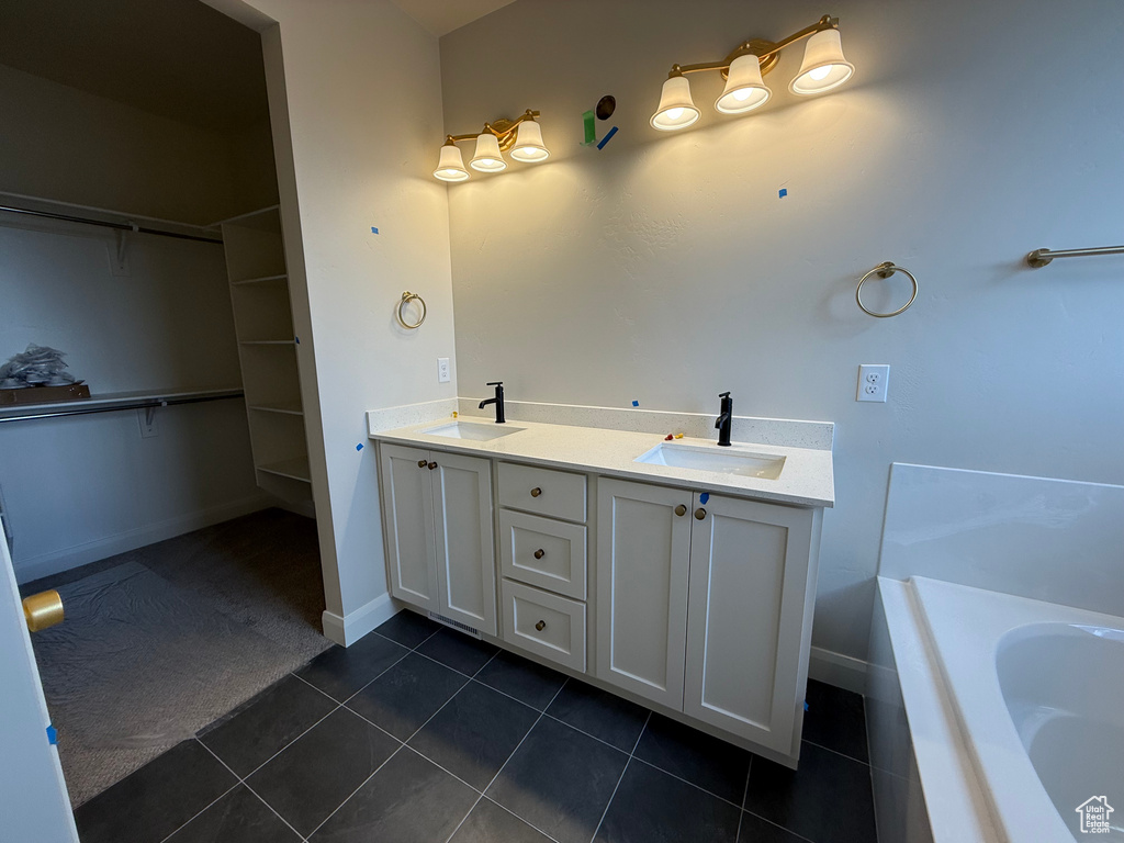 Bathroom featuring tile patterned floors, a spacious closet, baseboards, a tub, and double vanity