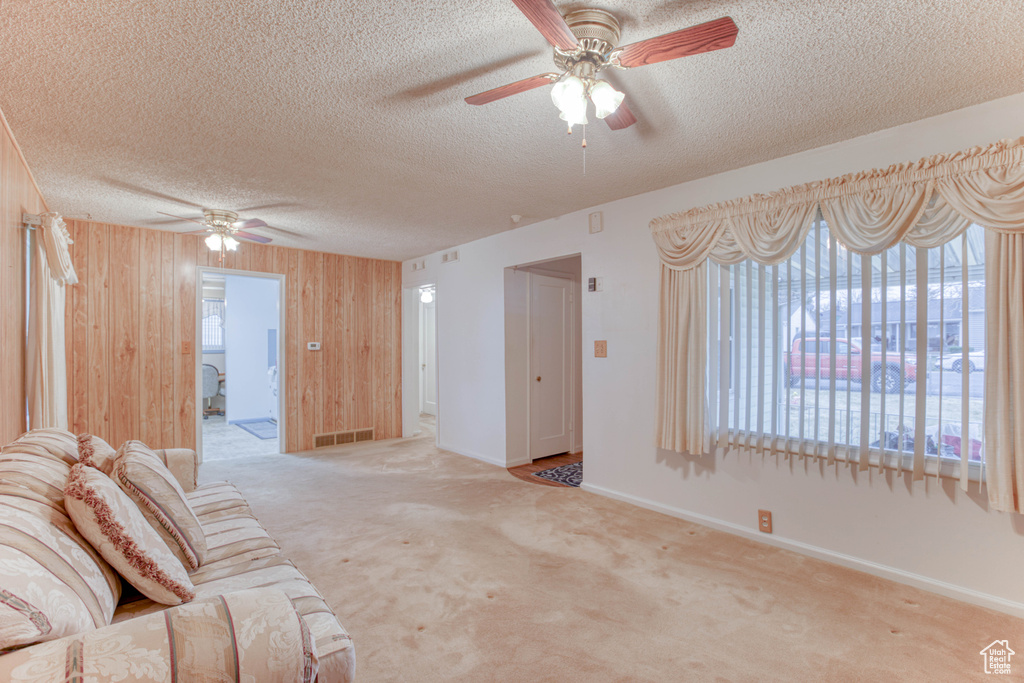 Living room featuring ceiling fan, light carpet, a textured ceiling, and wooden walls