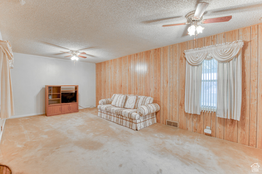 Unfurnished living room with ceiling fan, carpet floors, a textured ceiling, and wood walls