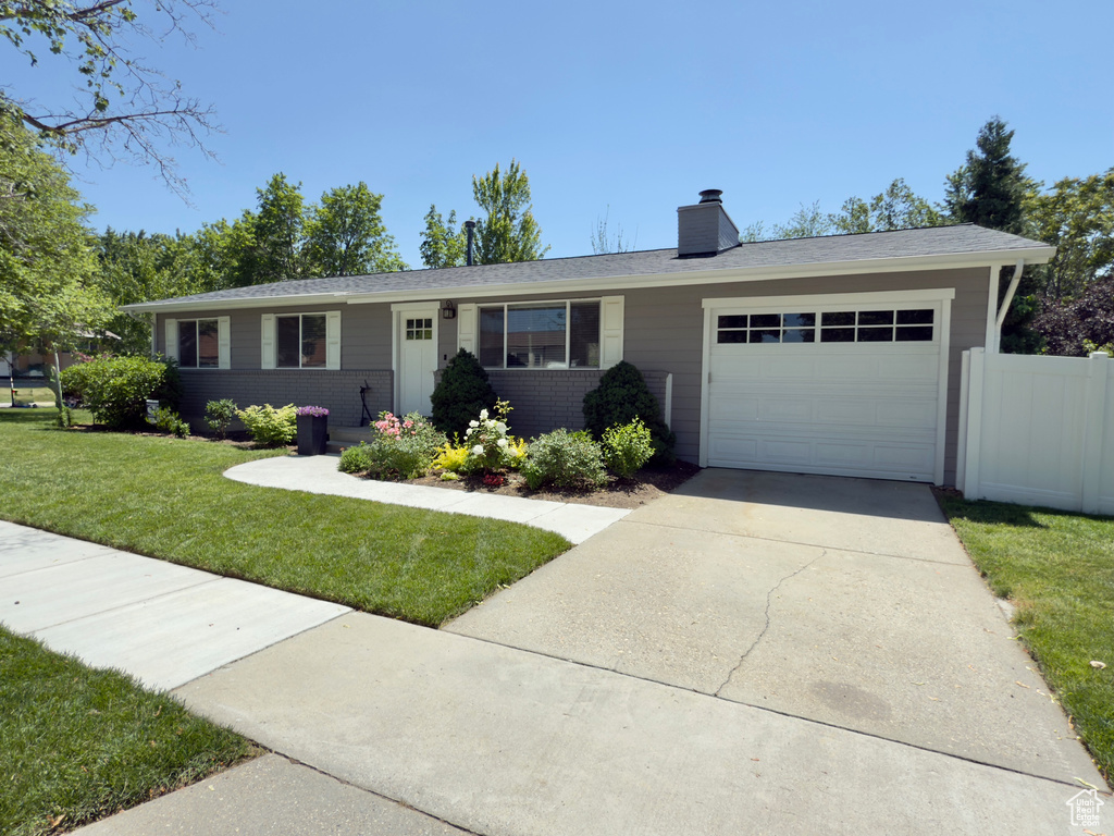 Ranch-style home with a garage, a chimney, driveway, and brick siding
