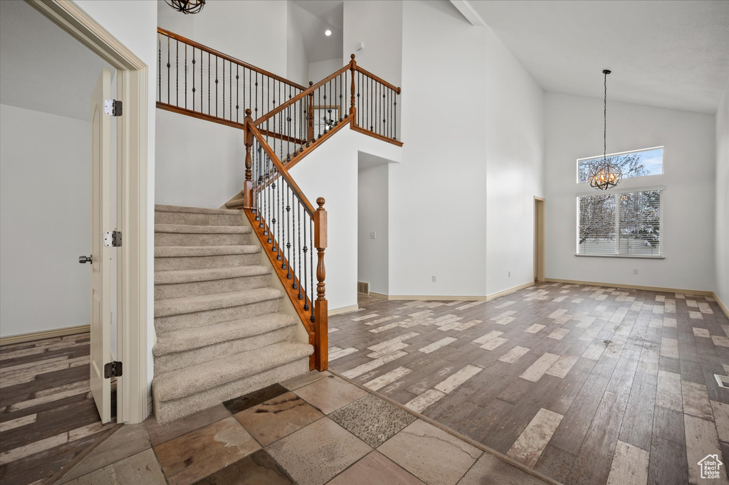 Staircase featuring an inviting chandelier, wood-type flooring, and high vaulted ceiling