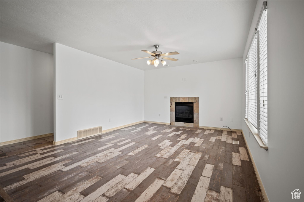 Unfurnished living room featuring a tiled fireplace, hardwood / wood-style flooring, and ceiling fan