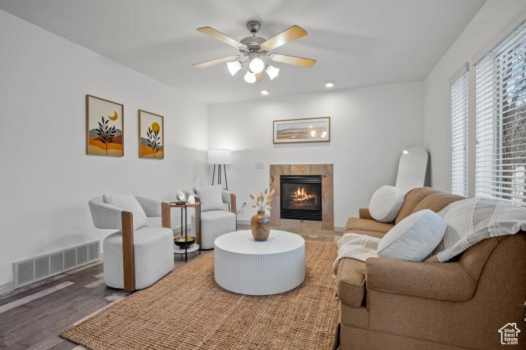 Living room featuring visible vents, wood finished floors, ceiling fan, and a tiled fireplace