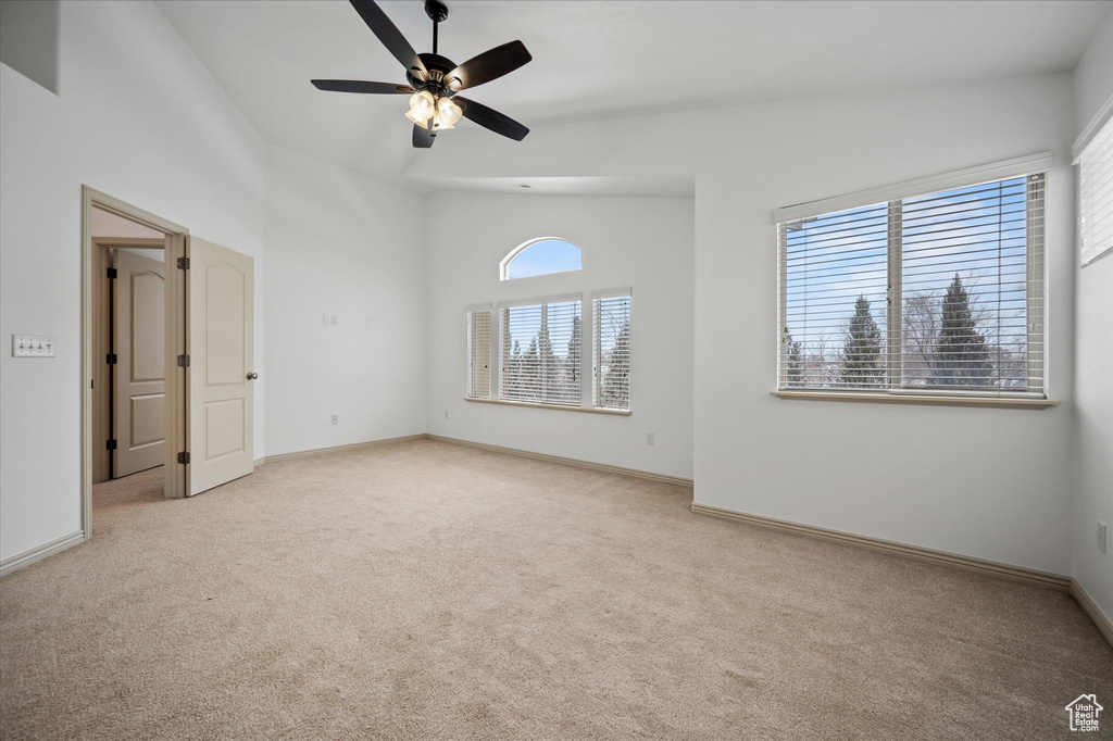 Carpeted empty room featuring vaulted ceiling and ceiling fan