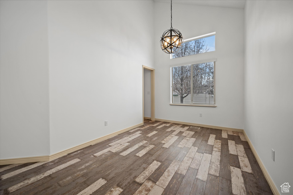 Spare room featuring an inviting chandelier, a towering ceiling, and wood-type flooring