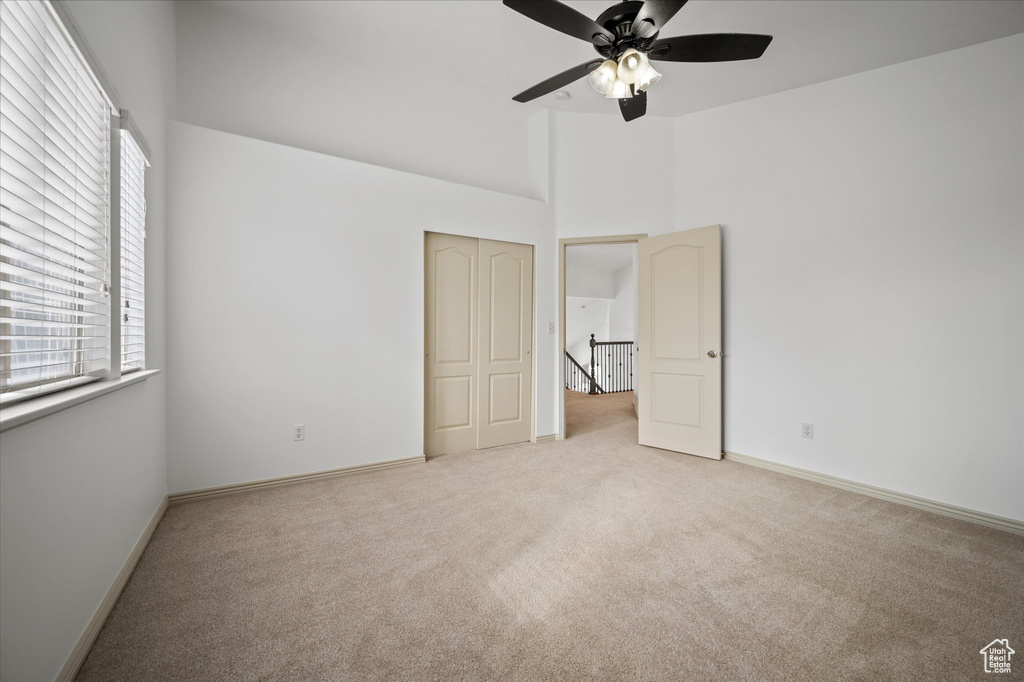 Unfurnished bedroom with a high ceiling, light colored carpet, ceiling fan, and a closet