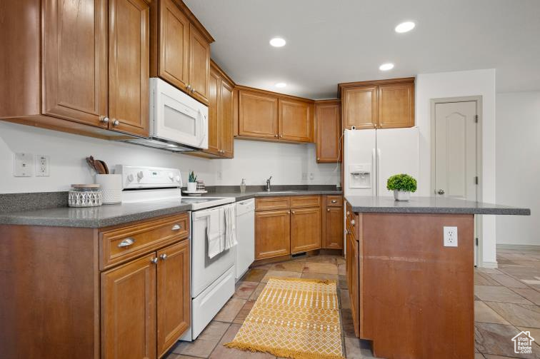 Kitchen featuring a center island, recessed lighting, brown cabinets, white appliances, and a sink