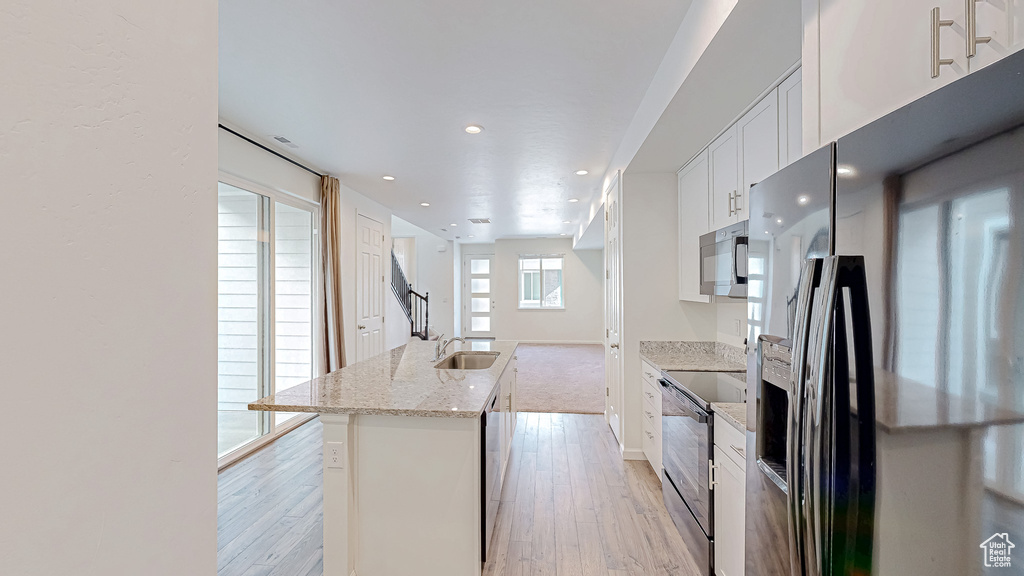 Kitchen with appliances with stainless steel finishes, white cabinetry, a center island, light stone counters, and light hardwood / wood-style floors