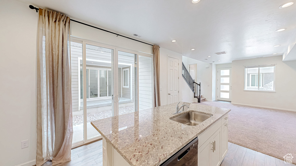 Kitchen featuring sink, a center island with sink, dishwasher, light stone countertops, and white cabinets