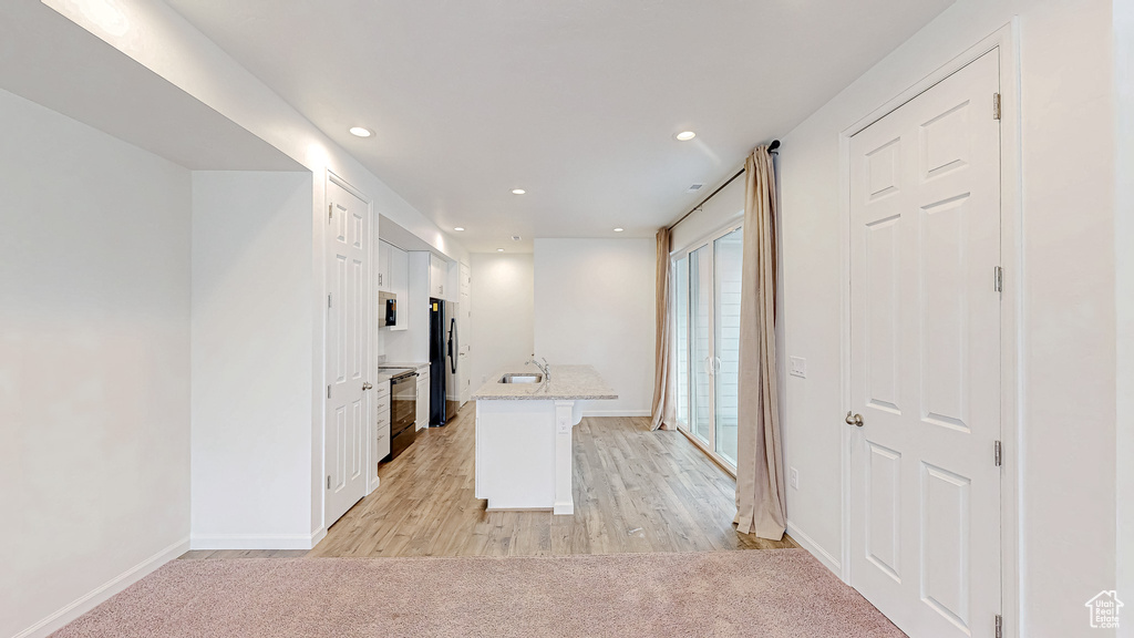 Kitchen featuring sink, white cabinetry, black fridge, light carpet, and kitchen peninsula