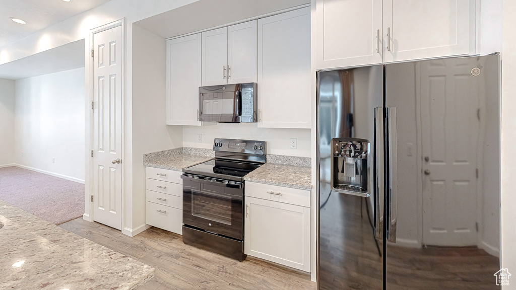 Kitchen featuring light hardwood / wood-style flooring, white cabinets, light stone counters, and black appliances