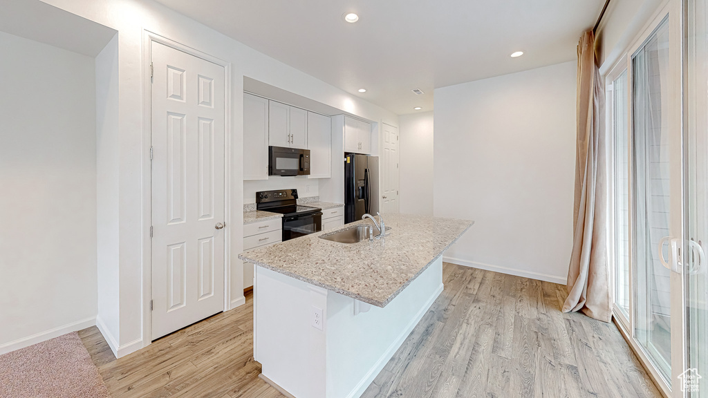 Kitchen featuring an island with sink, sink, white cabinets, black appliances, and light wood-type flooring