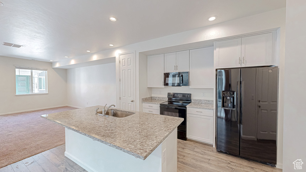 Kitchen with sink, black appliances, an island with sink, and white cabinets