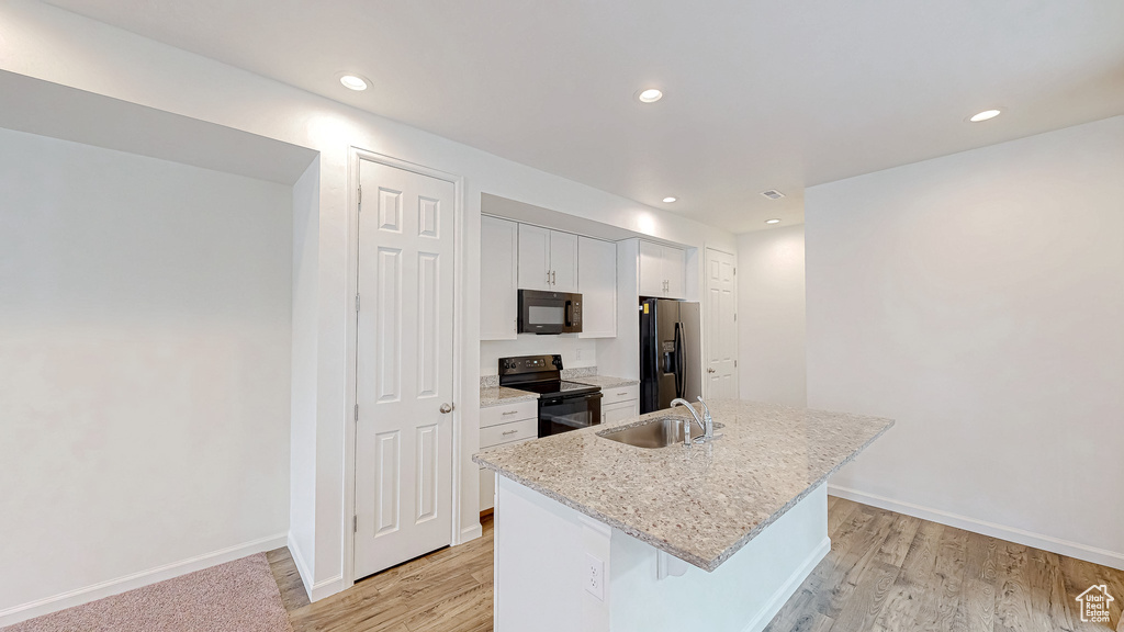 Kitchen featuring sink, a kitchen island with sink, light stone counters, black appliances, and white cabinets