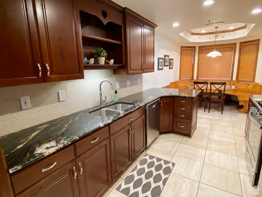 Kitchen featuring sink, dishwasher, dark stone countertops, hanging light fixtures, and kitchen peninsula