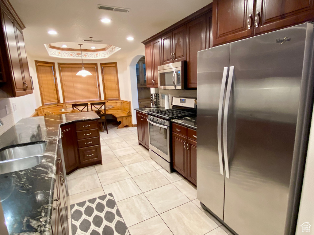 Kitchen featuring pendant lighting, sink, appliances with stainless steel finishes, a tray ceiling, and dark stone counters