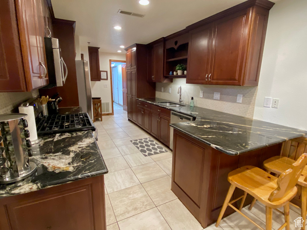 Kitchen featuring a breakfast bar, sink, dark stone counters, kitchen peninsula, and stainless steel appliances