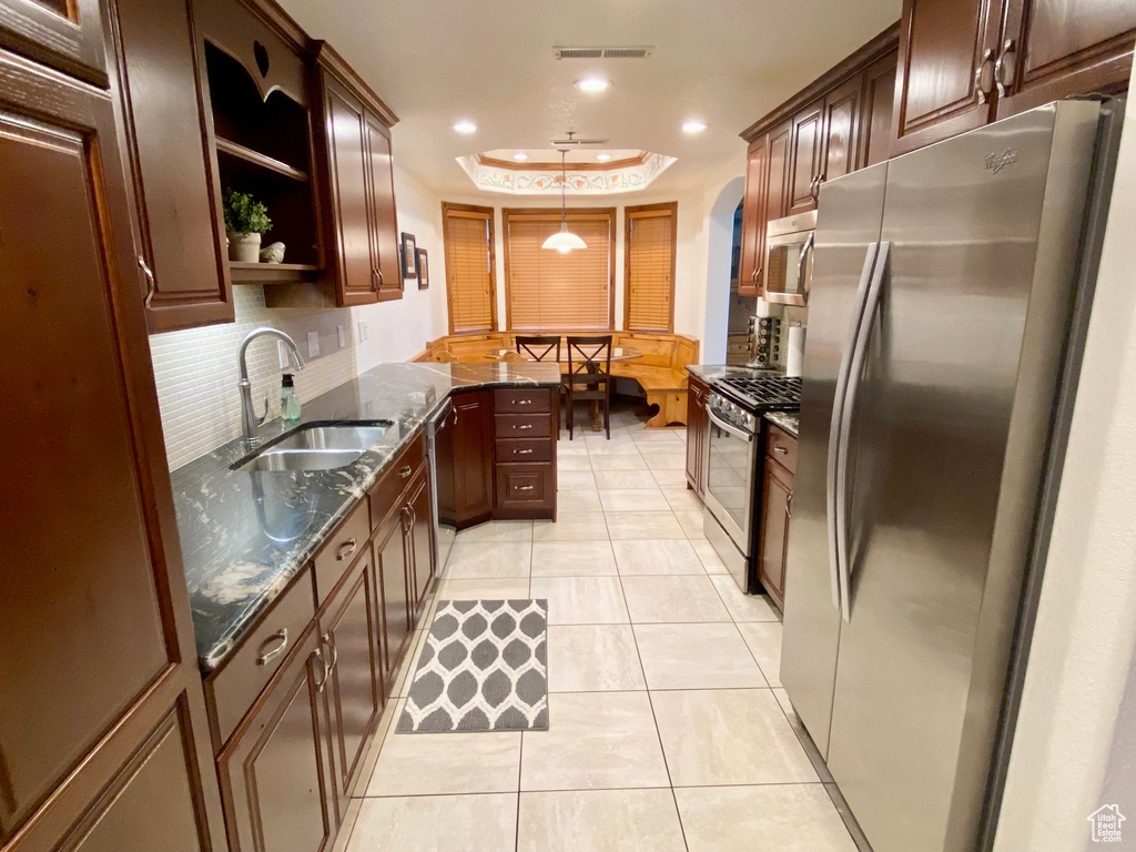 Kitchen featuring sink, tasteful backsplash, light tile patterned floors, a tray ceiling, and stainless steel appliances