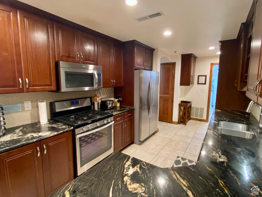 Kitchen with sink, dark stone countertops, backsplash, light tile patterned floors, and stainless steel appliances