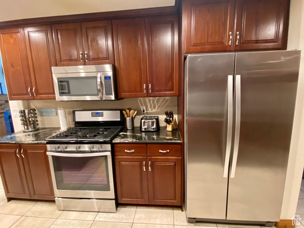 Kitchen with tasteful backsplash, appliances with stainless steel finishes, light tile patterned flooring, and dark stone counters