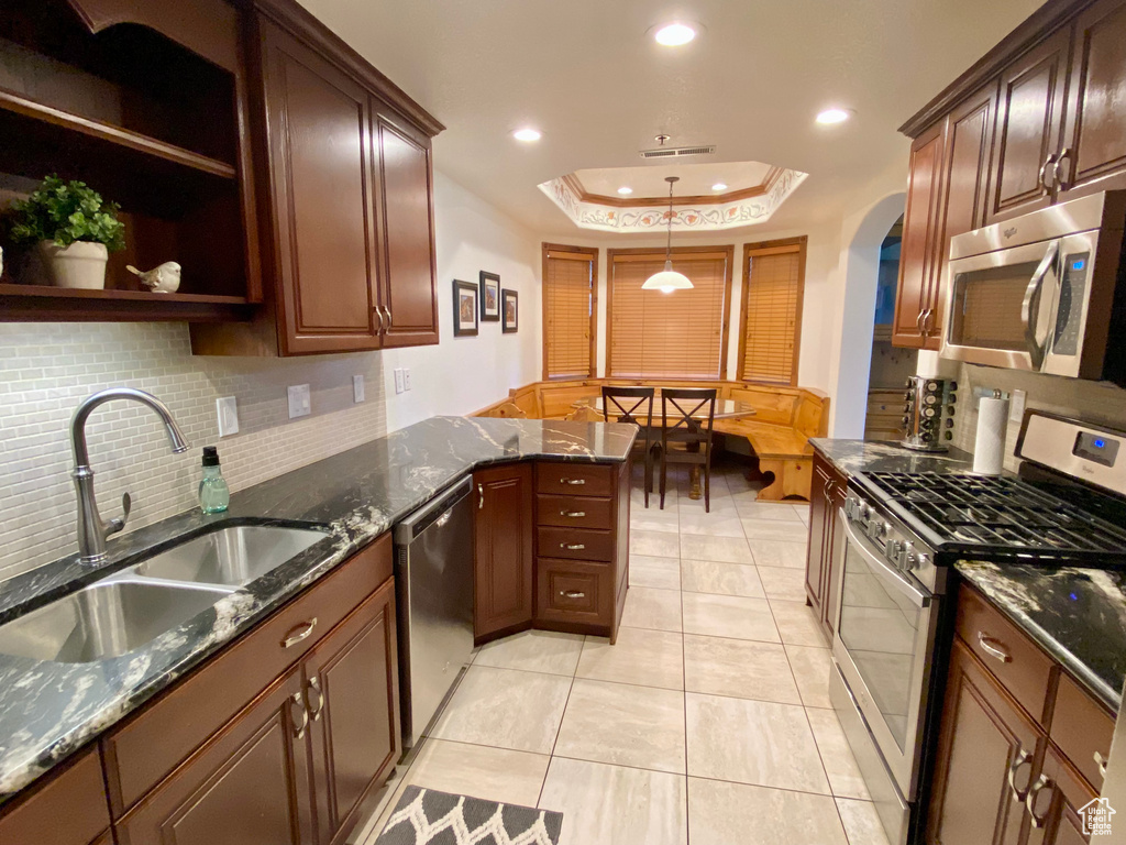 Kitchen with sink, a tray ceiling, stainless steel appliances, and dark stone counters