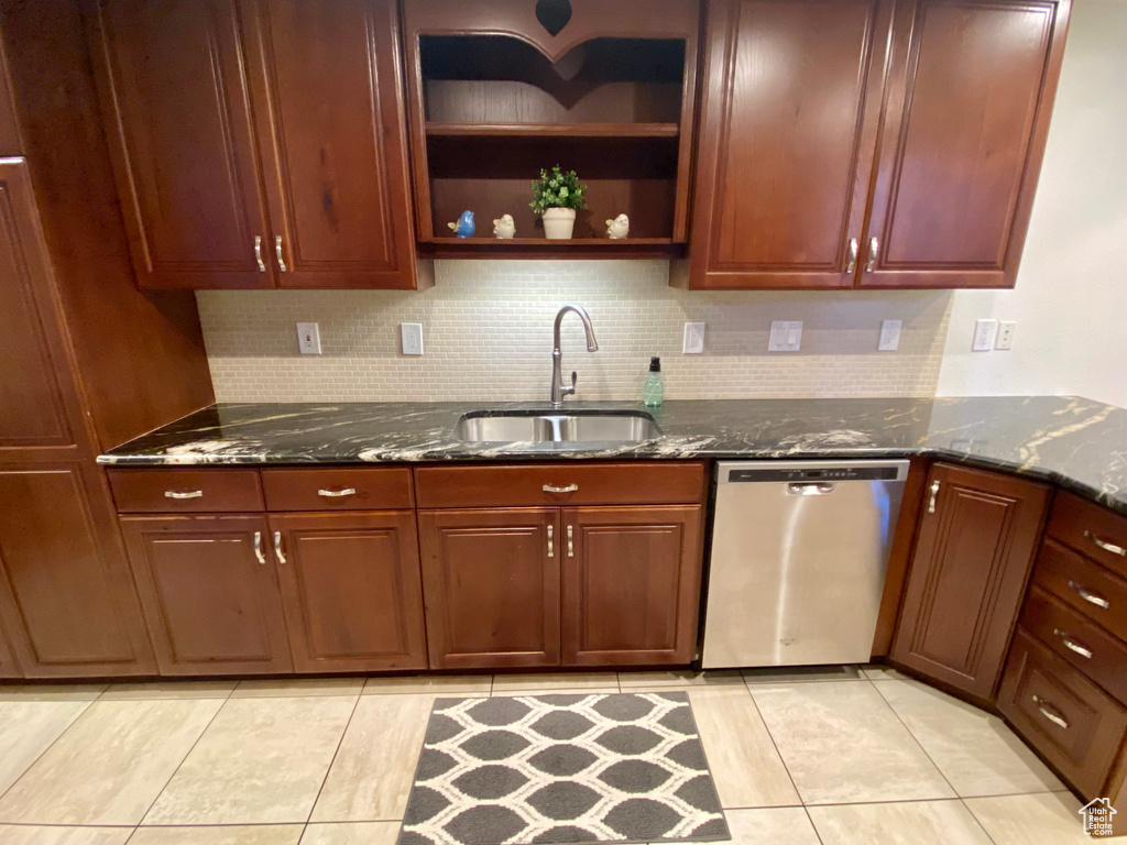 Kitchen featuring stainless steel dishwasher, sink, decorative backsplash, and dark stone countertops