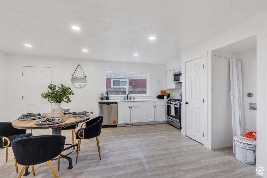 Kitchen with white cabinetry, sink, stainless steel appliances, and light wood-type flooring