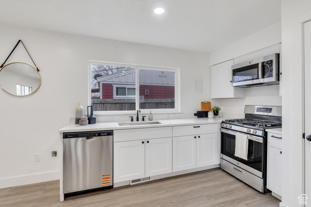 Kitchen with light wood-type flooring, stainless steel appliances, sink, and white cabinets