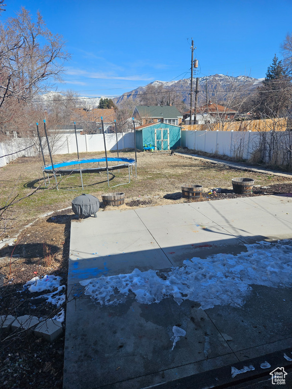 View of yard with a trampoline, a storage shed, a fenced backyard, an outbuilding, and a mountain view