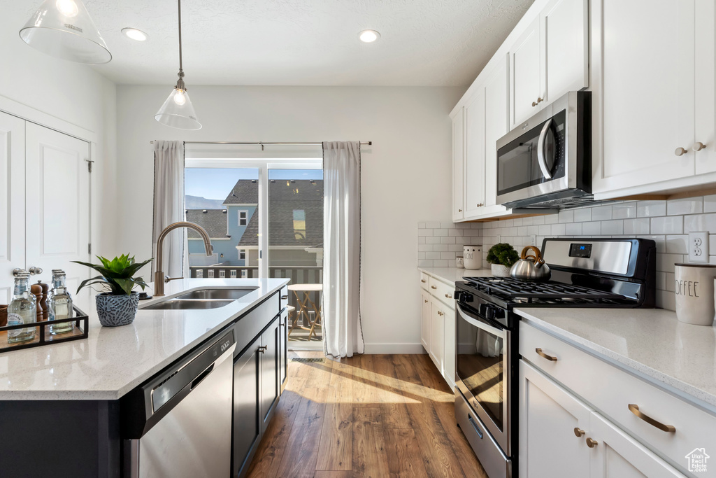 Kitchen featuring sink, backsplash, pendant lighting, stainless steel appliances, and white cabinets
