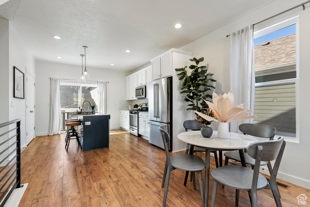 Kitchen with stainless steel appliances, a breakfast bar, a kitchen island, white cabinets, and pendant lighting