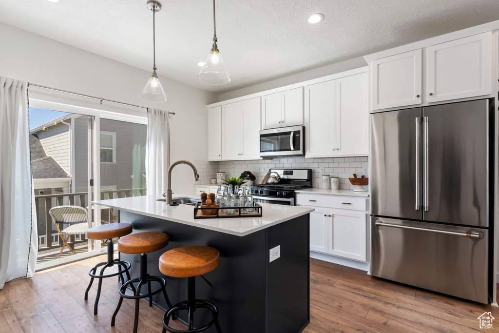 Kitchen with appliances with stainless steel finishes, an island with sink, hanging light fixtures, and white cabinets