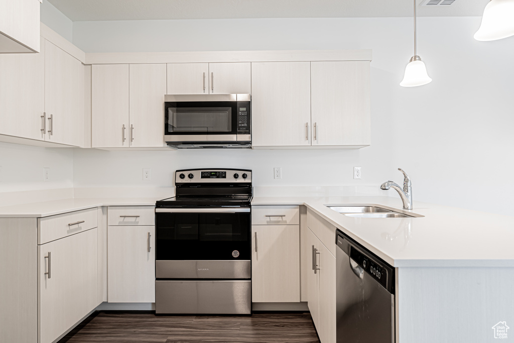 Kitchen with stainless steel appliances, a peninsula, dark wood-style flooring, light countertops, and pendant lighting