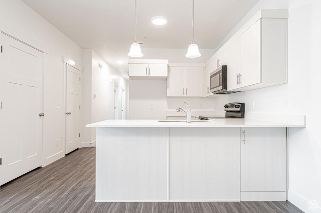 Kitchen with stove, a peninsula, dark wood finished floors, stainless steel microwave, and light countertops
