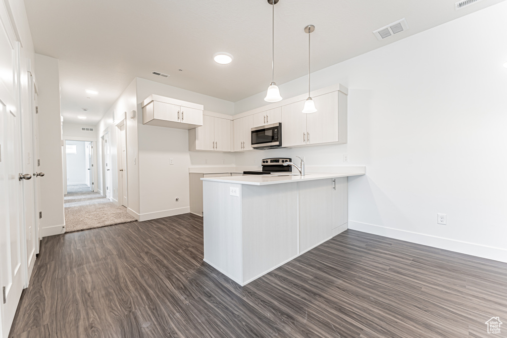 Kitchen featuring stainless steel microwave, a peninsula, electric stove, dark wood-style floors, and white cabinets