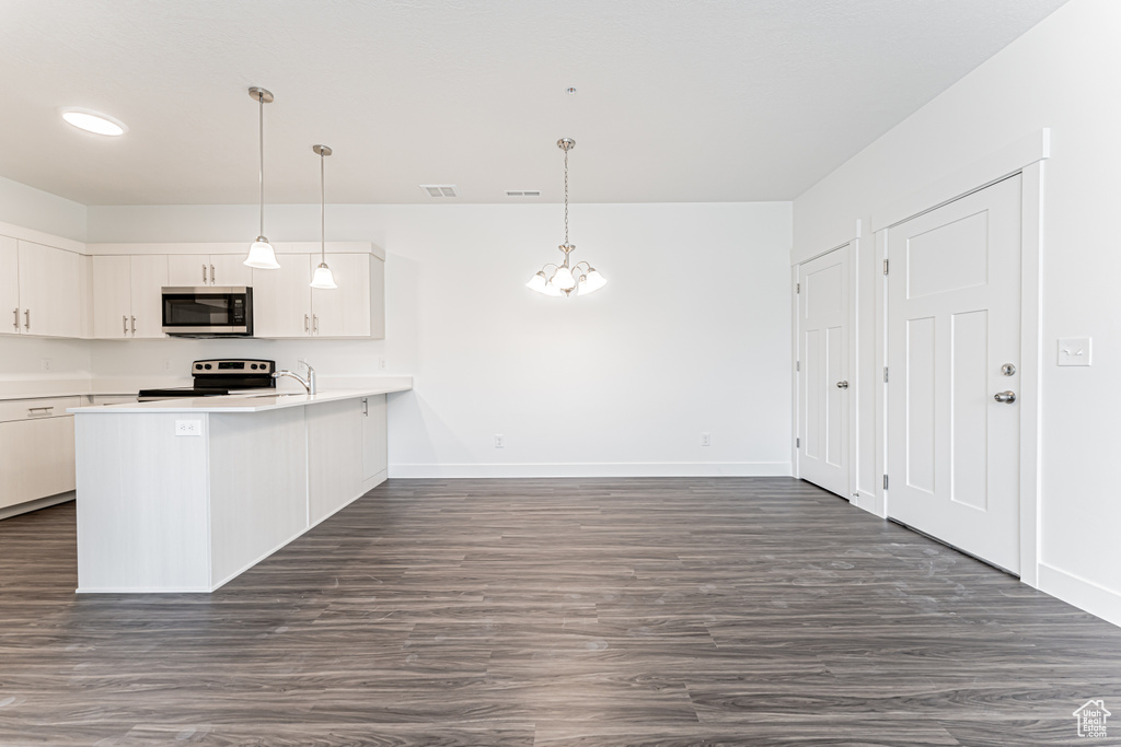 Kitchen with stainless steel microwave, electric range, light countertops, a peninsula, and white cabinetry