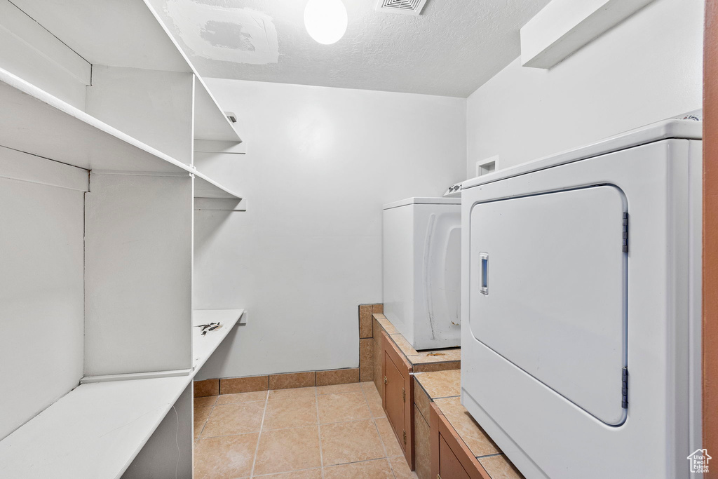 Laundry area featuring light tile patterned floors, a textured ceiling, and washer / dryer