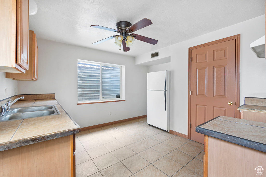 Kitchen with sink, white fridge, ceiling fan, and light tile patterned floors